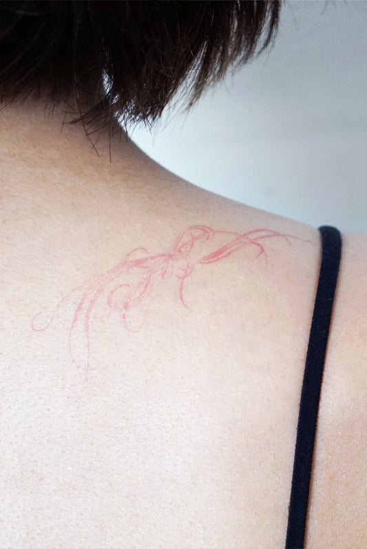 pink tattoo outline on a person's shoulder blade against a white background